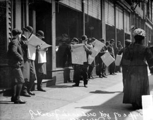 Image of job seekers, men standing in front of the Chicago Daily News building, looking at newspapers with pedestrians walking nearby. The building was located at 15 North Wells Street (formerly 123 Fifth Avenue) in the Loop community area of Chicago, Illinois. DN-0051332, Chicago Daily News negatives collection, Chicago History Museum.