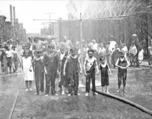 Image of a large group of children standing under showers over the street in Chicago, Illinois. Source: DN-0076144, Chicago Daily News negatives collection, Chicago History Museum.